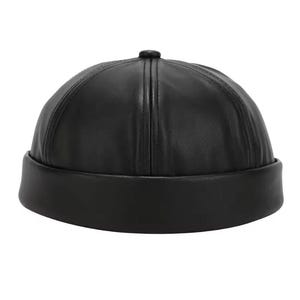 Può includere: Berretto in pelle nera con corona arrotondata e tesa corta e ripiegata. Il berretto ha un piccolo bottone rotondo sulla parte superiore e cuciture verticali. Il cappello è di colore nero pieno.