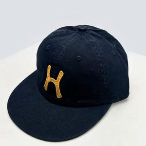 Peut inclure: Casquette de baseball bleu marine avec une visière incurvée. Le chapeau présente la lettre "H" dorée brodée sur le devant. Le chapeau est fait d'un tissu doux et durable.