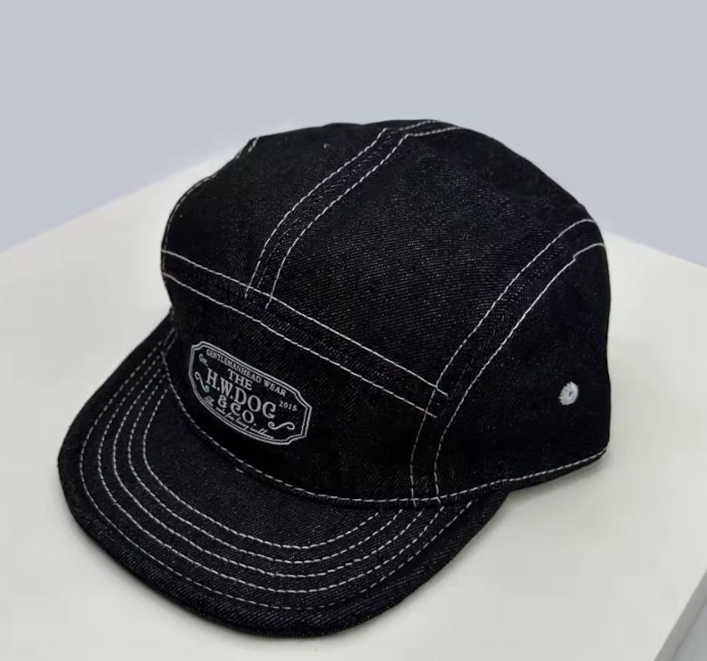 May include: Black denim cap with white stitching and a flat peak. The cap features a white patch with the text "GENTLEMAN HEAD WEAR THE H.W. DOG & CO. 2015". The cap has a five-panel design.
