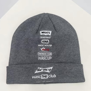 Peut inclure: Un bonnet gris avec plusieurs logos et du texte. Les logos incluent "WASC'S", "HIMYWAY", "HIWA", "WASC HOUSE", "THE WASC CLUB", "WASC UP", "Blue wasc up" et "wasc THE CLUB". Le bonnet est fait d'une matière tricotée douce.