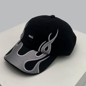 Może przedstawiać: Czarna czapka bejsbolowa z szarym wzorem płomieni na daszku i boku. Czapka ma napis "WASC" na małej kwadratowej naszywce. Czapka jest wykonana z miękkiego materiału i ma zakrzywiony daszek.