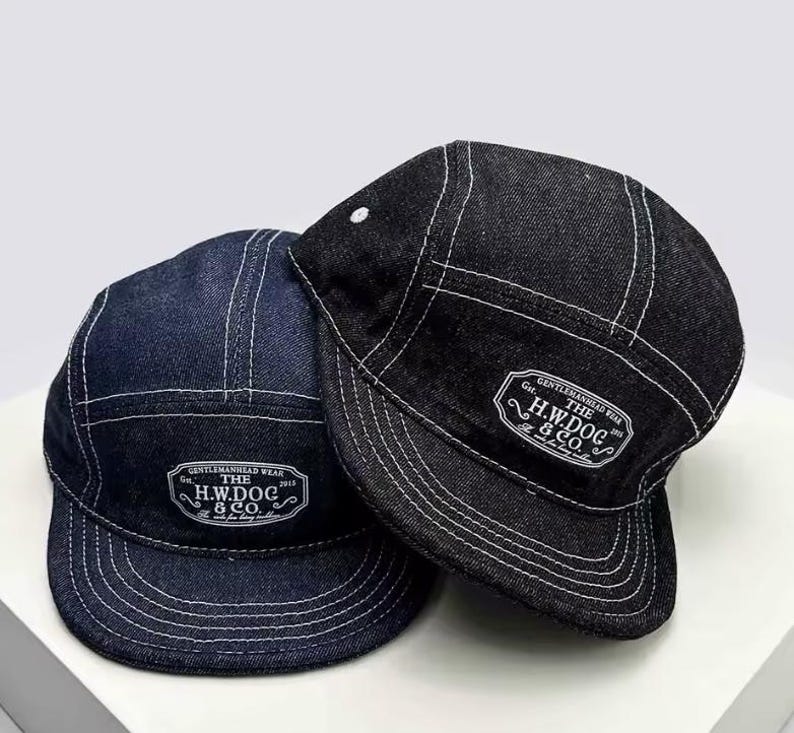 May include: Two denim caps, one dark blue and one black, with white stitching. Each cap has a white label with the text "THE H.W.DOG & CO." and "GENTLEMANHEAD WEAR". The caps have a classic, five-panel design.