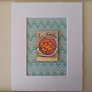 May include: A framed art print featuring a colorful illustration of a concha pastry on a plate. The artwork, titled "La Concha," showcases the pastry with orange and yellow details. The background has a teal and white geometric pattern.