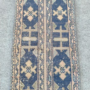 Könnte beinhalten: Ein langer, schmaler Läufer mit tiefblauem Hintergrund und sich wiederholenden geometrischen Mustern in gedecktem Pfirsich, Salbeigrün und Creme. Das Design besteht aus vertikalen Streifen mit stilisierten Blumenmotiven und Bordüren.