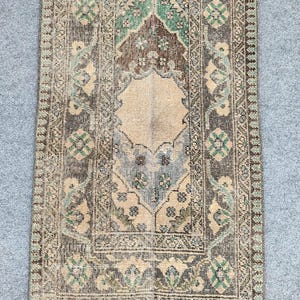 Könnte beinhalten: Rechteckiger Teppich im Used-Look mit einem zentralen Medaillon-Design. Der Teppich weist eine Farbpalette aus Braun, Beige und Grün auf, mit komplizierten floralen und geometrischen Mustern. Die Ränder sind mit einem detaillierten Design eingefasst.