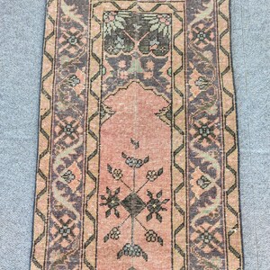 Könnte beinhalten: Ein rechteckiger Teppich im Vintage-Stil mit einem zentralen rosa Feld und aufwendigen Bordürendesigns. Der Teppich weist ein Blumenmuster in Rosa-, Grün-, Schwarz- und Beigetönen auf. Das Design des Teppichs ist symmetrisch, mit einem zentralen Medaillon und sich wiederholenden Mustern.