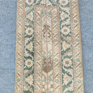 Könnte beinhalten: Ein rechteckiger Teppich im Vintage-Stil mit zentralem Design und Bordüre. Der Teppich hat einen beigefarbenen Hintergrund mit einem braunen und teal-farbenen zentralen Design. Die Bordüre ist eine Mischung aus Beige, Braun und Teal mit floralen und geometrischen Mustern.