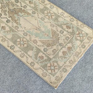 May include: An antique-style rug with a rectangular shape. The rug features a beige background with intricate patterns in shades of green, brown, and light blue. The border has a detailed floral design. The rug is likely made of woven material.