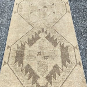 May include: Beige and brown patterned runner rug. The rug features a central diamond design with geometric shapes and a border of repeating patterns. The colour palette is neutral, with light beige and brown tones, creating a warm aesthetic.