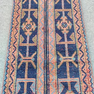 Peut inclure: Un tapis rectangulaire à motifs avec un fond bleu marine et des motifs géométriques en pêche, bleu clair et vert olive. Le tapis présente une bande centrale et des bordures avec des motifs répétitifs. Le tapis est probablement utilisé comme chemin de couloir.