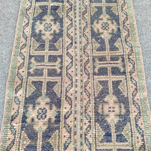 May include: A rectangular rug with a symmetrical design. The rug features a central navy blue pattern with geometric shapes and floral motifs, bordered by light green and beige accents. The rug's design is repeated on both sides.