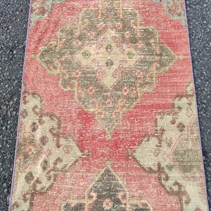 May include: A rectangular, distressed rug with a central medallion design. The rug features a faded red background with accents of brown, beige, and teal. The pattern is geometric and traditional, suitable for home decor.