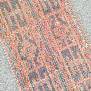 Peut inclure: Un tapis de couloir rectangulaire présentant un motif géométrique répétitif dans des tons de gris anthracite, corail sourd et turquoise vif. Le design se compose de blocs interconnectés et de bordures linéaires à poils tissés.