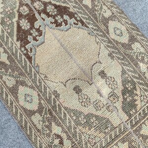 Könnte beinhalten: Ein antiker Teppich mit einem zentralen beigen Medaillon und aufwendigen Blumenmustern in Braun, Grün und Blau-Grau. Der Rand des Teppichs weist ein sich wiederholendes geometrisches Design auf. Der Teppich ist gefaltet und zeigt seine strukturierte Webart.