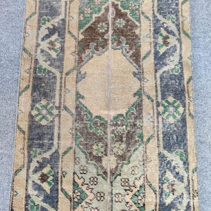 Könnte beinhalten: Ein rechteckiger Teppich im Vintage-Stil mit einem Used-Look. Der Teppich hat ein beiges Mittelfeld mit komplizierten Mustern in Blau, Grün und Braun. Das Design umfasst florale und geometrische Motive und erzeugt eine klassische, gealterte Ästhetik.