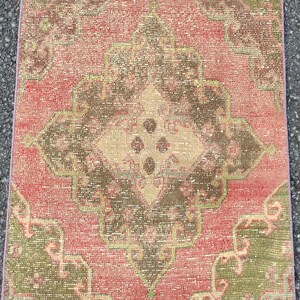 May include: A rectangular, distressed rug with a central medallion design. The rug features a faded colour palette of red, brown, and green, with a beige centre. The rug's edges are a lighter shade of pink.