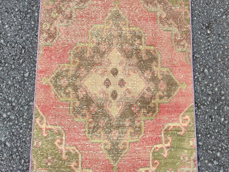May include: A rectangular, distressed rug with a central medallion design. The rug features a faded colour palette of red, brown, and green, with a beige centre. The rug's edges are a lighter shade of pink.