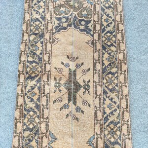 May include: A rectangular, vintage rug with a central beige field and detailed borders. The rug displays a symmetrical design with floral and geometric patterns in brown, blue, and beige. The rug's dimensions are not visible.