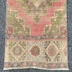 May include: A rectangular, distressed rug with a faded, vintage appearance. The rug features a central field of red and green, with intricate floral and geometric patterns. The border has a diamond and floral design in muted tones.