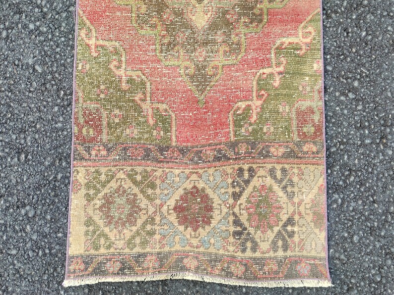 May include: A rectangular, distressed rug with a faded, vintage appearance. The rug features a central field of red and green, with intricate floral and geometric patterns. The border has a diamond and floral design in muted tones.