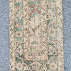 Könnte beinhalten: Ein rechteckiger Vintage-Teppich mit einem Used-Look. Der Teppich hat ein zentrales Design in Beige, Grün und Braun mit floralen und geometrischen Mustern. Die Ränder sind mit einem dunkleren Grün- und Beigemuster eingefasst.