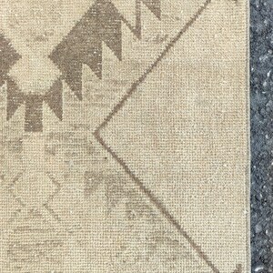 May include: Close-up of a beige and brown patterned rug. The rug features geometric designs, including zigzags and diamond shapes, in shades of brown against a beige background. The rug has a textured surface and a neutral colour palette.