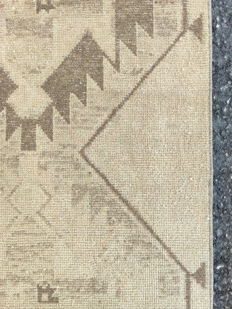 May include: Close-up of a beige and brown patterned rug. The rug features geometric designs, including zigzags and diamond shapes, in shades of brown against a beige background. The rug has a textured surface and a neutral colour palette.