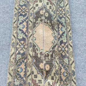 Op de afbeelding: Een antiek loperkleed met een versleten, vintage uitstraling. Het kleed heeft een centraal ontwerp in bruin- en beigetinten, omlijst door ingewikkelde patronen in blauw, groen en rood. Het ontwerp is symmetrisch, met een vervaagde, verouderde uitstraling.