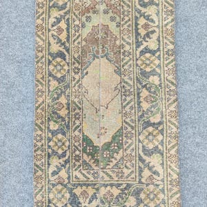 Peut inclure: Tapis rectangulaire de style vintage avec un motif central beige, vert et marron. La bordure présente un motif floral répétitif dans les tons de bleu, beige et vert. Le tapis a un aspect vieilli.