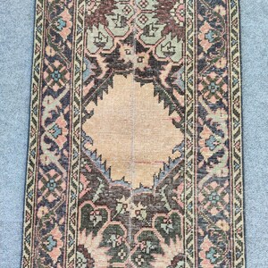 Könnte beinhalten: Ein rechteckiger, antiker Teppich mit einem zentralen Rautenmuster in Beige, umgeben von aufwendigen floralen und geometrischen Mustern in Braun, Grün, Blau und Rosa. Der Teppich hat ein abgenutztes Aussehen, was auf Alter und Gebrauch hindeutet.