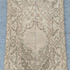 Könnte beinhalten: Ein rechteckiger Vintage-Teppich mit einem zentralen Medaillon-Design. Der Teppich hat eine Farbpalette aus Beige, Braun und gedämpftem Grün mit komplizierten floralen und geometrischen Mustern. Die Ränder des Teppichs sind mit dunklerem Braun eingefasst.
