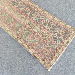 May include: A rectangular, vintage-style rug with a distressed look. The rug has a repeating pattern in pink, green, and blue, with a beige border. The rug's dimensions are not visible.