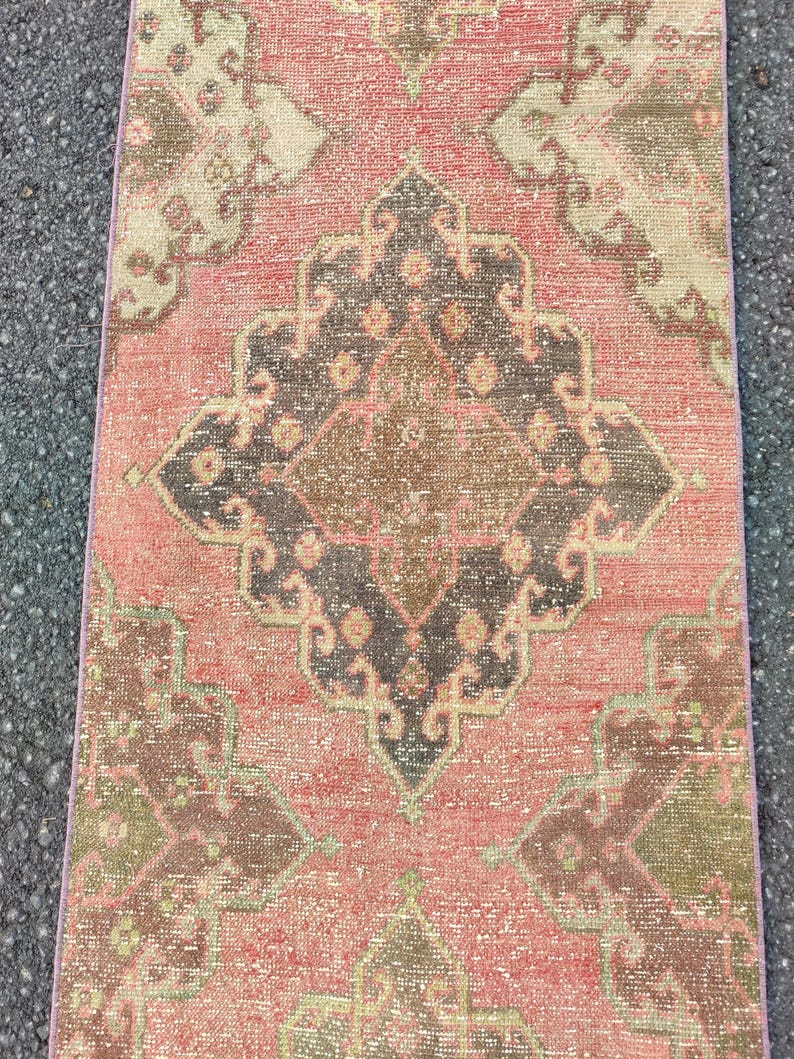 May include: A rectangular, distressed rug with a central medallion design. The rug features a faded colour palette of coral, brown, and olive green. The pattern includes geometric shapes and floral motifs, creating a vintage aesthetic.