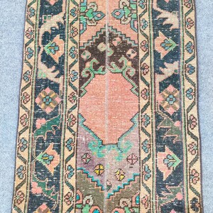 Könnte beinhalten: Ein rechteckiger Vintage-Teppich mit einem zentralen pfirsichfarbenen Feld und dunkelblauen Bordüren. Der Teppich weist komplizierte Blumen- und geometrische Muster in Grün-, Rosa- und Brauntönen auf und erzeugt einen Used-Look.