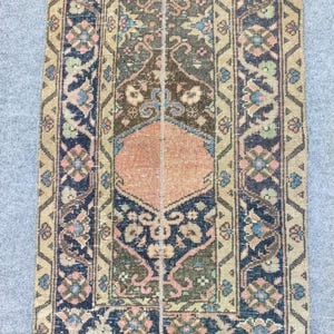 May include: A rectangular, vintage rug with a central design in shades of brown, peach, and green. The rug features intricate floral patterns and a navy blue border with additional floral motifs. The overall aesthetic is a blend of classic and rustic.