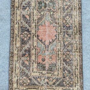 Könnte beinhalten: Rechteckiger Teppich im Used-Look mit einem zentralen Blumendesign in Pfirsich- und Türkistönen. Der Teppich hat einen dunkelbraunen und olivgrünen Rand und Hintergrund, was ihm einen Vintage-Look verleiht. Geeignet für die Inneneinrichtung.