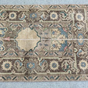 Peut inclure: Tapis ancien avec un motif géométrique détaillé. Le tapis présente un champ central beige avec une bordure marron foncé. Des touches de bleu et de turquoise sont incorporées dans le design, créant une esthétique vintage.