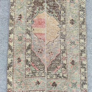 Op de afbeelding: Een rechthoekig vloerkleed in vintage-stijl met een centraal medaillonontwerp. Het vloerkleed heeft een palet van gedempte kleuren, waaronder beige, bruin, roze en groen. De randen zijn afgezet met bloemmotieven en het vloerkleed heeft een versleten uitstraling.