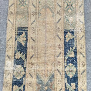 May include: A rectangular, vintage-style rug with a central beige field and vertical stripes. The rug features floral and geometric patterns in shades of blue, green, and brown. The rug's design includes a dark blue border with floral motifs.