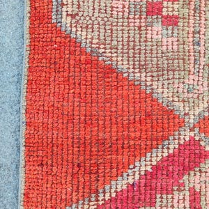 May include: Close-up of a section of a hand-woven rug. The rug features a vibrant color palette, with a prominent area of bright red and accents of pink, gray, and blue. The texture is dense and appears to be made of wool.