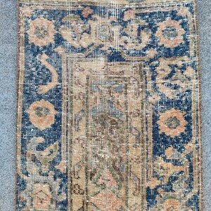 Könnte beinhalten: Ein rechteckiger Vintage-Teppich mit einem beigen Mittelfeld und einem dunkelblauen Rand. Der Teppich weist florale und geometrische Muster in Beige-, Pfirsich- und Blautönen auf. Der Teppich hat ein abgenutztes Aussehen, das auf Alter und Gebrauch hindeutet.