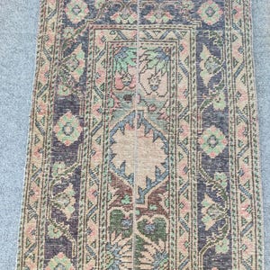 May include: A rectangular area rug featuring a central beige medallion surrounded by intricate geometric and floral patterns in shades of navy blue, sage green, and soft pink. The border displays a repeating diamond motif with floral accents.