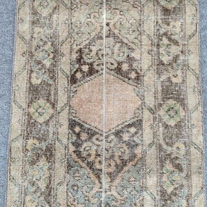 Könnte beinhalten: Ein rechteckiger Teppich im Vintage-Stil mit einem Used-Look. Der Teppich hat ein zentrales Design in Braun-, Beige- und Blassrosatönen mit floralen und geometrischen Mustern. Die Ränder und Bordüren sind dunkler.