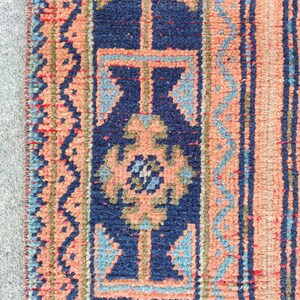 Peut inclure: Gros plan sur une section d'un tapis à motifs géométriques. Le tapis présente un motif central bleu marine avec des accents pêche et bleu clair. La bordure présente un motif à rayures pêche et bleu. Le tapis a un aspect texturé.