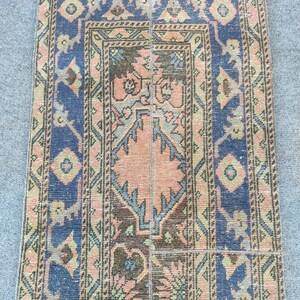 May include: A rectangular, vintage rug with a central design in peach and brown, framed by a navy blue border. The rug features intricate floral and geometric patterns in shades of peach, blue, and green.