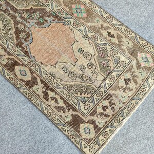 May include: Rectangular, vintage-style rug with a central peach-coloured medallion and intricate border. The rug features a distressed design with brown, beige, and muted green tones, creating a warm aesthetic. The rug's dimensions are not visible.