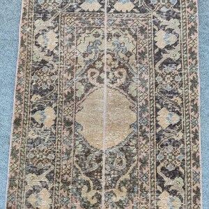 Peut inclure: Un tapis rectangulaire et vieilli avec un médaillon central beige et des motifs floraux complexes dans des tons de marron, vert et bleu. Le tapis a un aspect vintage délavé, avec une bordure rose.