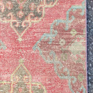 May include: Close-up of a section of a vintage rug with a distressed, faded appearance. The rug features a red background with intricate patterns in grey, light blue, and beige. The design has a traditional, ornate style.