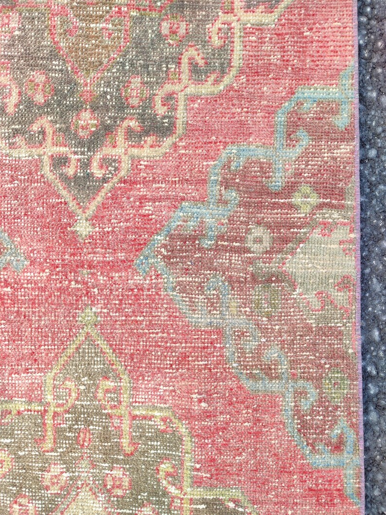 May include: Close-up of a section of a vintage rug with a distressed, faded appearance. The rug features a red background with intricate patterns in grey, light blue, and beige. The design has a traditional, ornate style.