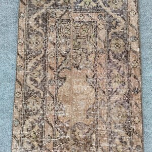Könnte beinhalten: Ein rechteckiger Vintage-Teppich mit abgenutztem Aussehen. Der Teppich hat ein zentrales Medaillon-Design in Braun-, Beige- und Olivgrüntönen. Aufwendige Blumen- und geometrische Muster bedecken die Oberfläche und schaffen eine traditionelle Ästhetik. Die Kanten des Teppichs sind leicht ausgefranst.